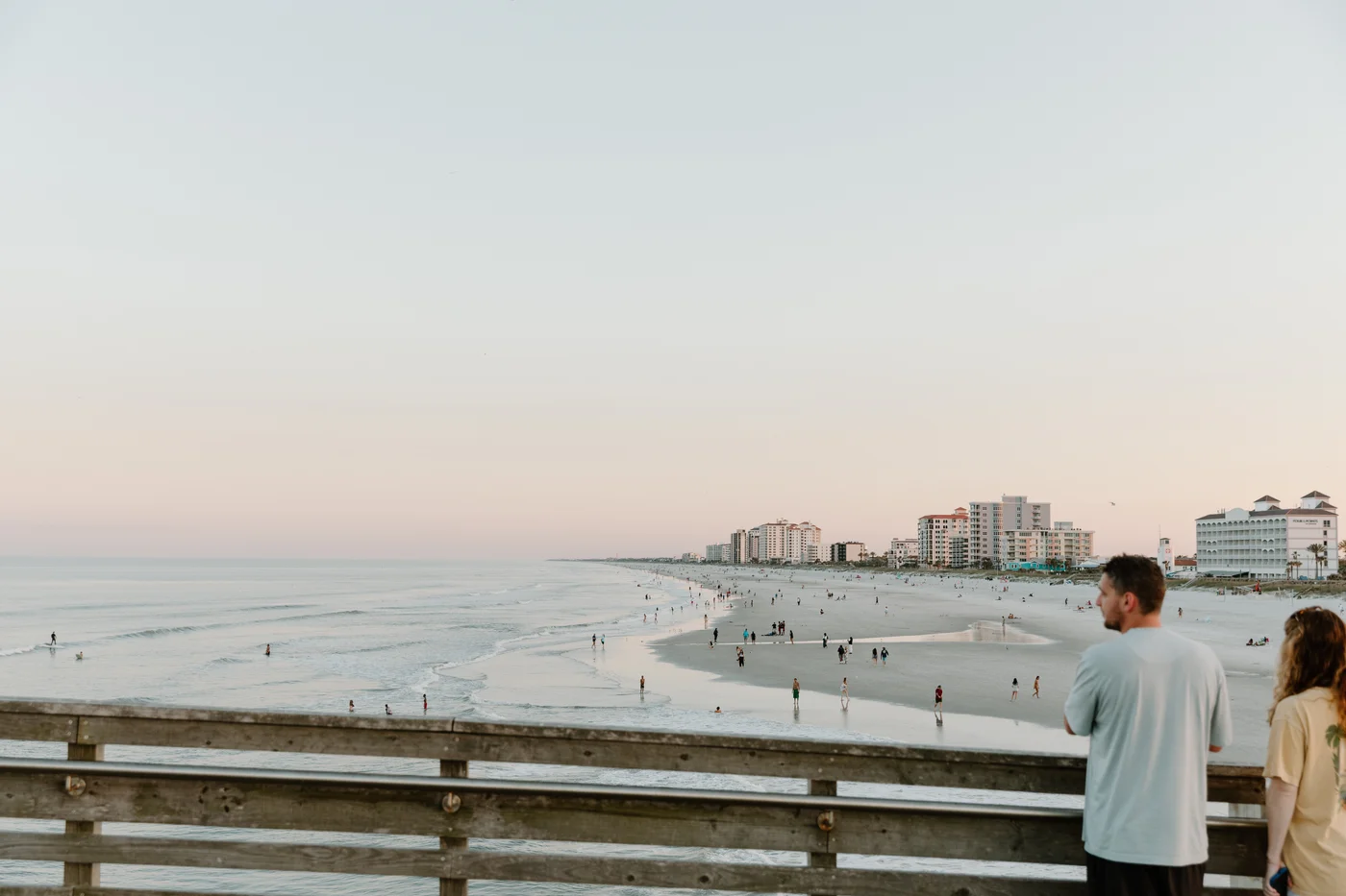 People looking out from a pier over a beach and coastal buildings