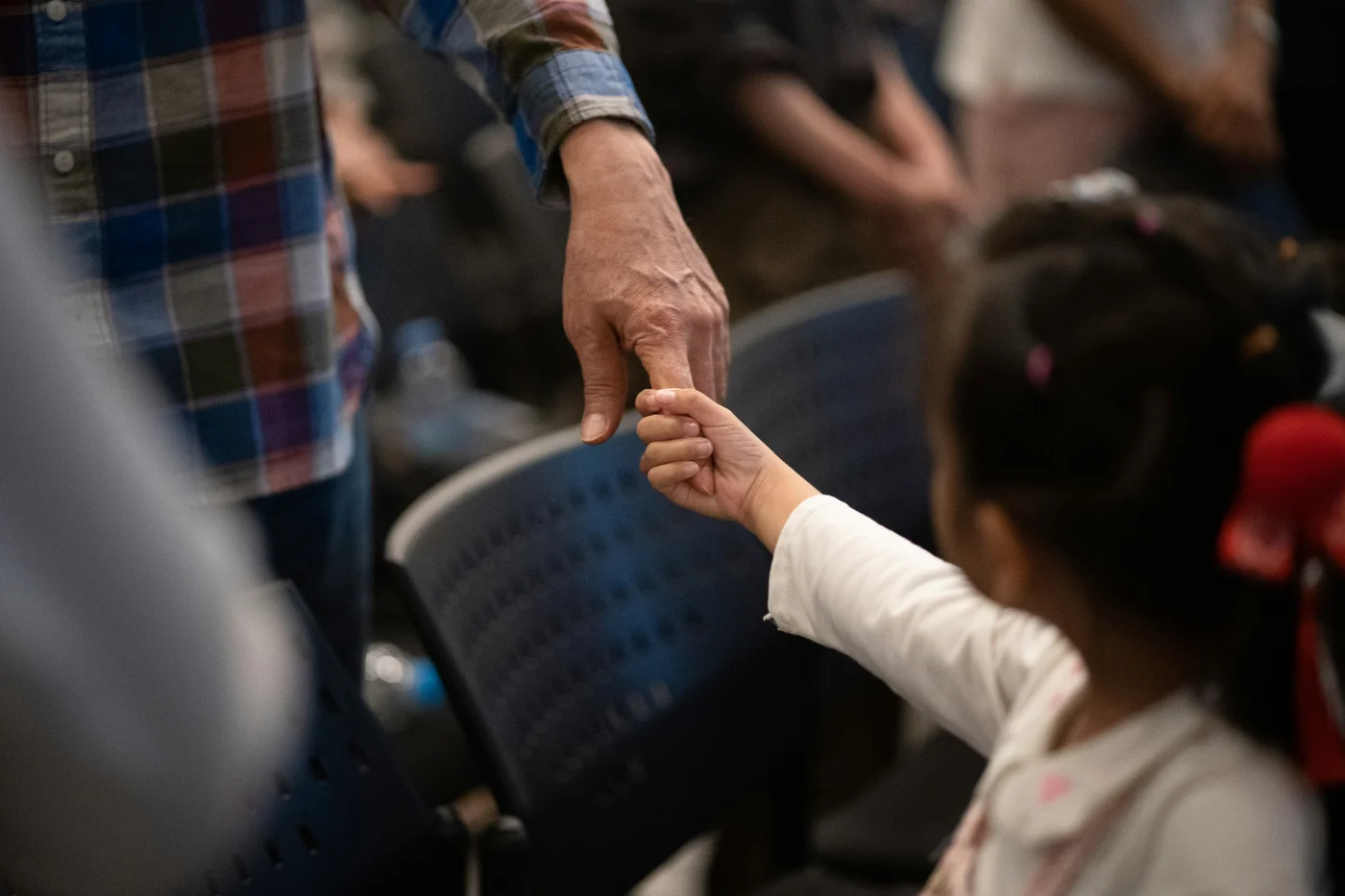 A child holding an adult’s hand beside rows of chairs