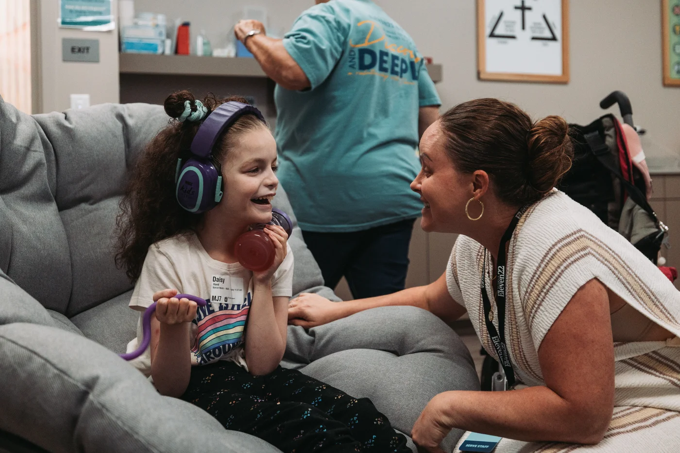 A volunteer smiling with a seated child wearing headphones